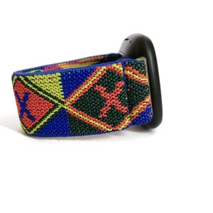 May include: A black watch with a colorful patterned strap. The strap is made of woven fabric and features a geometric design in shades of red, yellow, blue, and green.