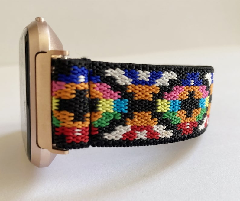 May include: A rose gold smartwatch with a black and multi-colored patterned elastic band.