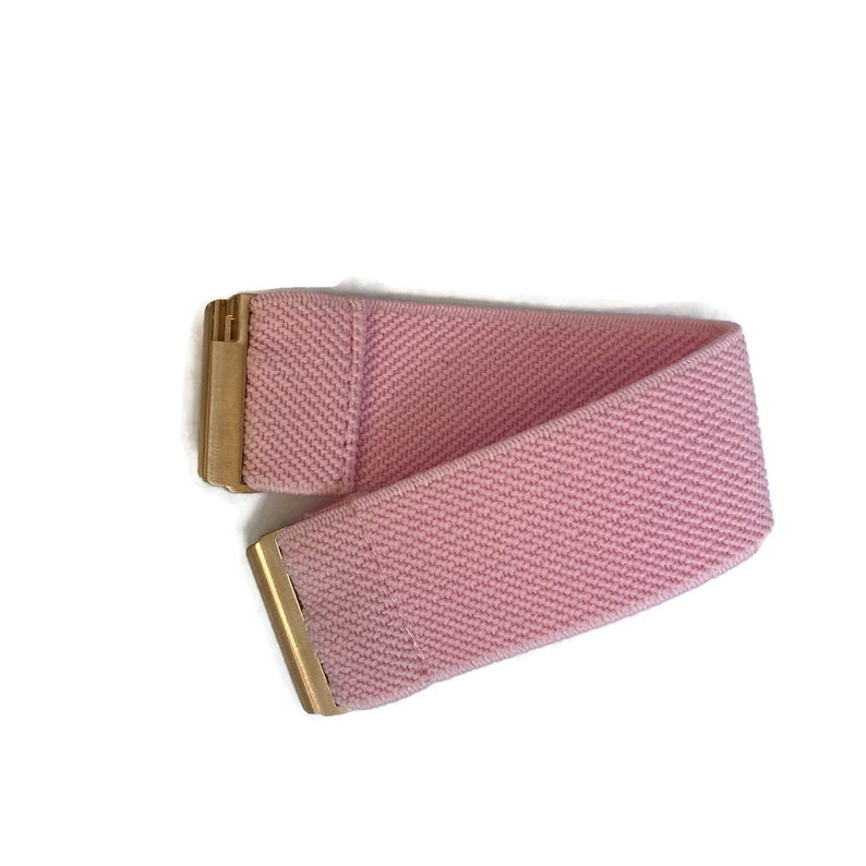 May include: A pink elastic belt with a gold buckle. The belt is made of a soft, stretchy material and is perfect for adding a touch of colour to any outfit.