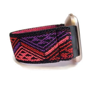 Puede incluir: Una correa de reloj con estampado negro, rosa y morado con una esfera de reloj de oro rosa.