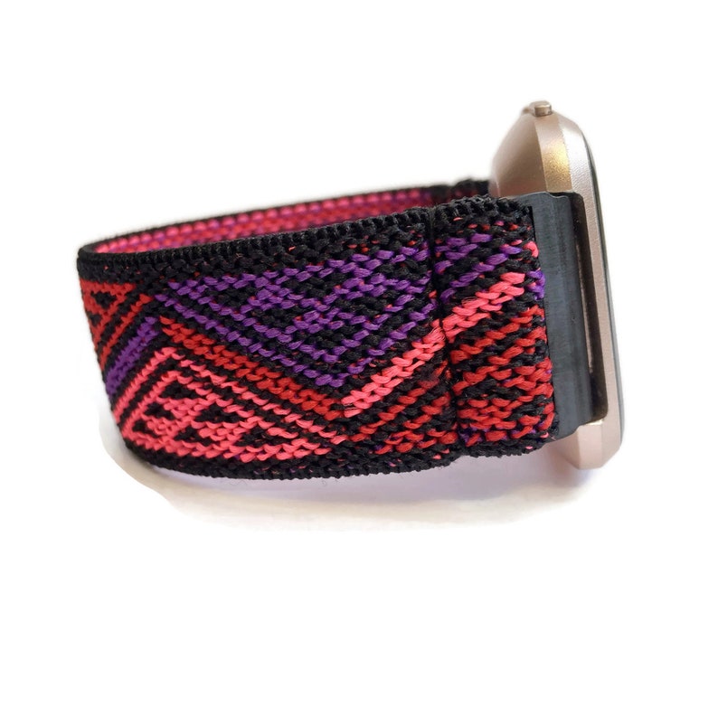 Puede incluir: Una correa de reloj con estampado negro, rosa y morado con una esfera de reloj de oro rosa.