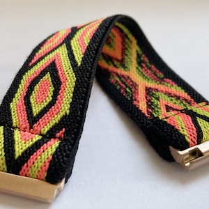 May include: A black elastic watch band with a geometric pattern in pink and green. The band has a gold metal clasp.