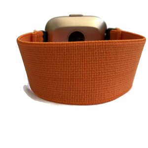 K&ouml;nnte beinhalten: Orangefarbenes elastisches Armband mit silbernem Zifferblatt.