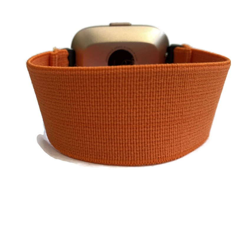 K&ouml;nnte beinhalten: Orangefarbenes elastisches Armband mit silbernem Zifferblatt.