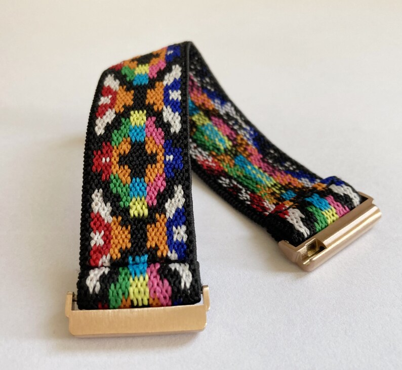 May include: A black elastic watch band with a colorful geometric pattern and gold metal clasps.
