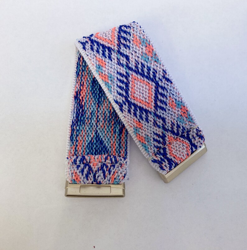 May include: A white elastic watch band with a blue, pink, and white geometric pattern.