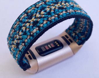 Puede incluir: Un rastreador de fitness de color dorado con una banda estampada en azul, negro y blanco. La banda tiene un diseño geométrico.