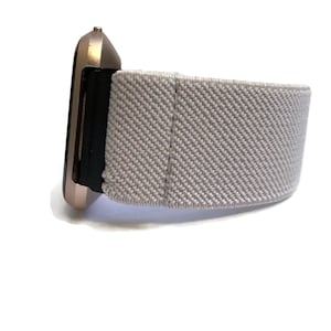 May include: A rose gold smartwatch with a gray fabric band. The band is made of a soft, breathable material and is designed for comfort.