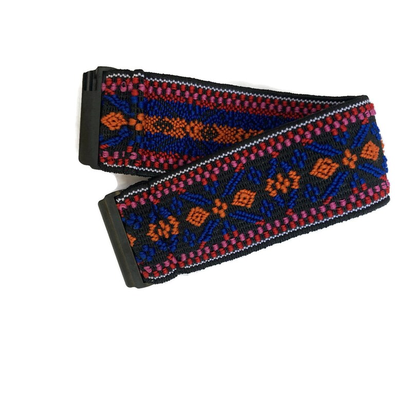 Op de afbeelding: Een zwart elastiek met een kleurrijk geometrisch patroon in tinten rood, oranje, blauw en roze. Het elastiek heeft een zwarte gesp.