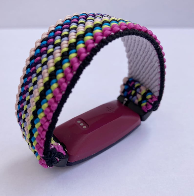 Op de afbeelding: Een kleurrijk geweven band met roze, blauwe, gele en zwarte strepen. Het band is bevestigd aan een bordeauxrode fitness tracker.