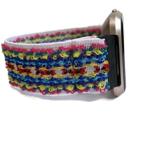 May include: A white watch strap with a colourful woven pattern. The strap is made of a soft, stretchy material and is compatible with most smartwatches.