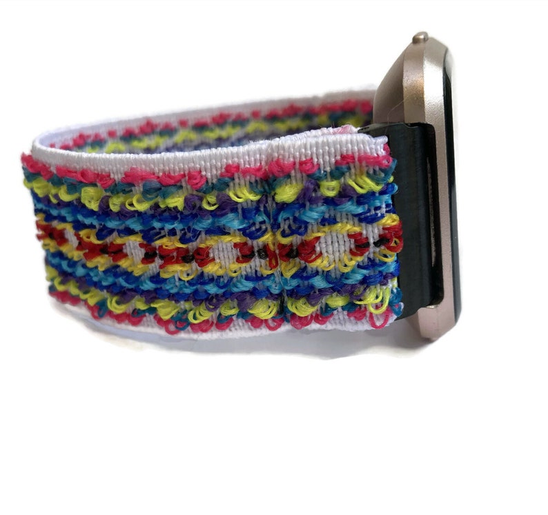 May include: A white watch strap with a colourful woven pattern. The strap is made of a soft, stretchy material and is compatible with most smartwatches.