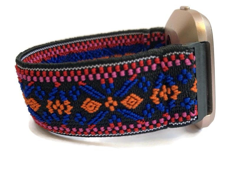 Op de afbeelding: Een zwart horlogebandje met een kleurrijk geometrisch patroon in rood, oranje, blauw en roze. Het bandje is gemaakt van elastisch materiaal en heeft een zilveren horlogekast.