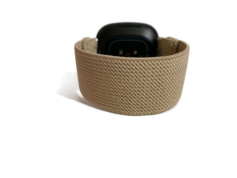 K&ouml;nnte beinhalten: Ein beigefarbenes Sportarmband f&uuml;r eine Smartwatch. Das Armband besteht aus einem weichen, dehnbaren Material und hat eine strukturierte Oberfl&auml;che.