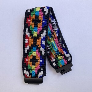 May include: A colourful woven elastic band with black accents and metal clasps. The band features a geometric pattern in shades of red, orange, yellow, green, blue, and white.