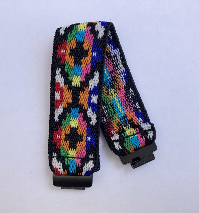 May include: A colourful woven elastic band with black accents and metal clasps. The band features a geometric pattern in shades of red, orange, yellow, green, blue, and white.