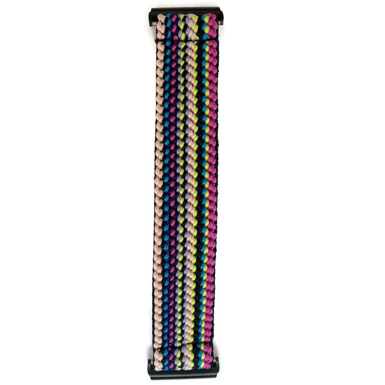May include: A colourful striped woven watch band with black metal clasps. The band is made of a soft, stretchy material and features a variety of colours, including pink, blue, green, and yellow.