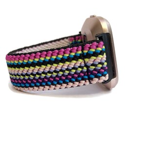May include: A colourful woven watch band with pink, blue, yellow and black stripes. The band is attached to a silver smartwatch.