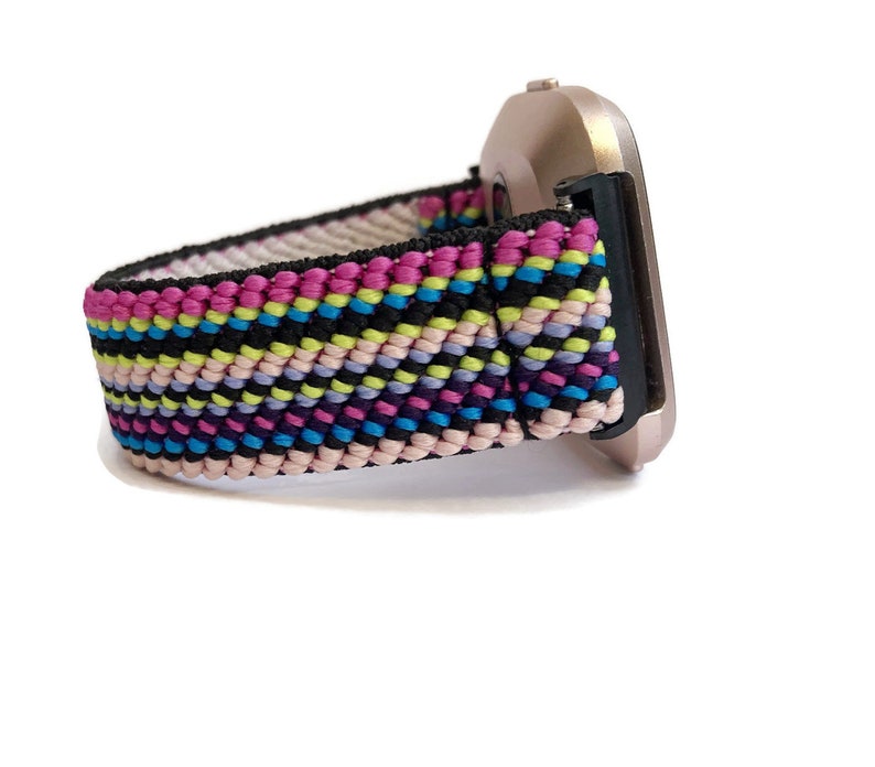 May include: A colourful woven watch band with pink, blue, yellow and black stripes. The band is attached to a silver smartwatch.