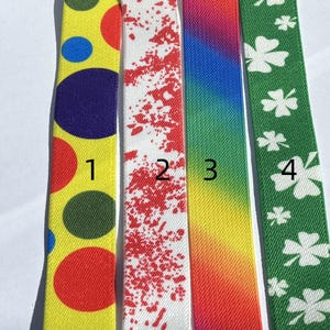 May include: Four colorful ribbons. The first is yellow with red, blue, and green circles. The second is white with red splatters. The third is a rainbow gradient. The fourth is green with white shamrocks.