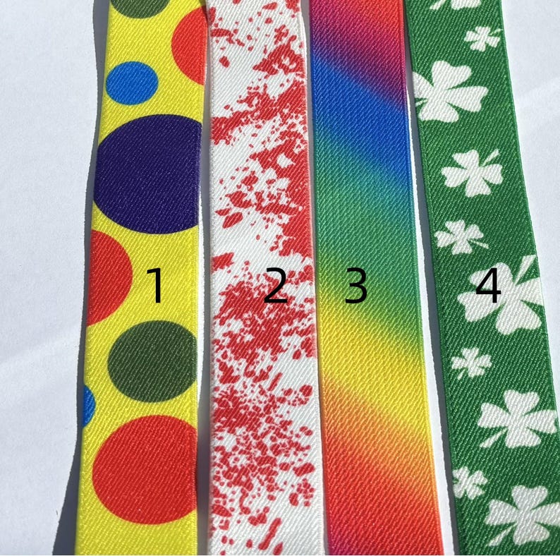 May include: Four colorful ribbons. The first is yellow with red, blue, and green circles. The second is white with red splatters. The third is a rainbow gradient. The fourth is green with white shamrocks.