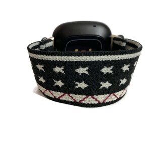 May include: Black fitness tracker with a white and black patterned band. The band has a white star pattern and a red and white diamond pattern.