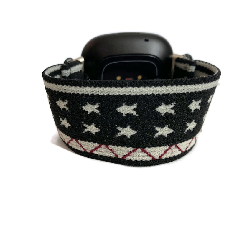 May include: Black fitness tracker with a white and black patterned band. The band has a white star pattern and a red and white diamond pattern.