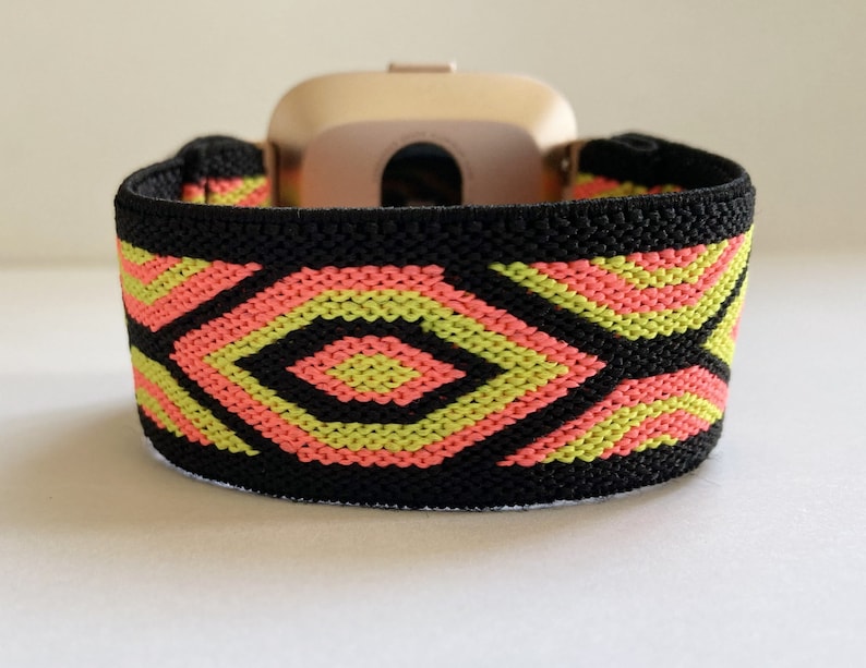 May include: Black elastic watch band with a geometric pattern in pink and green. The band is designed to fit a smartwatch.