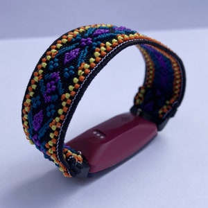 May include: A black fitness tracker band with a colorful geometric pattern in shades of orange, yellow, blue, and purple. The band is attached to a burgundy fitness tracker.