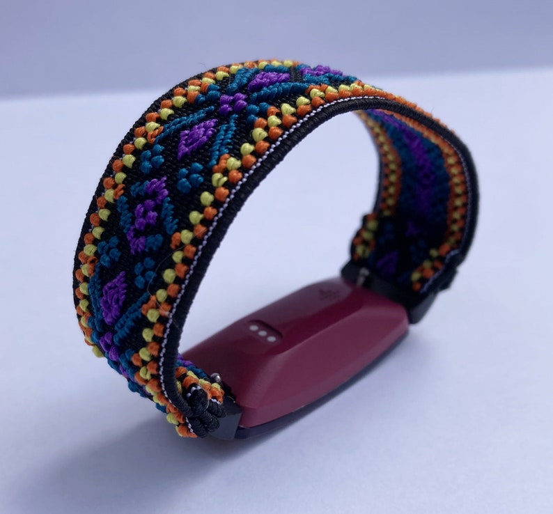 May include: A black fitness tracker band with a colorful geometric pattern in shades of orange, yellow, blue, and purple. The band is attached to a burgundy fitness tracker.