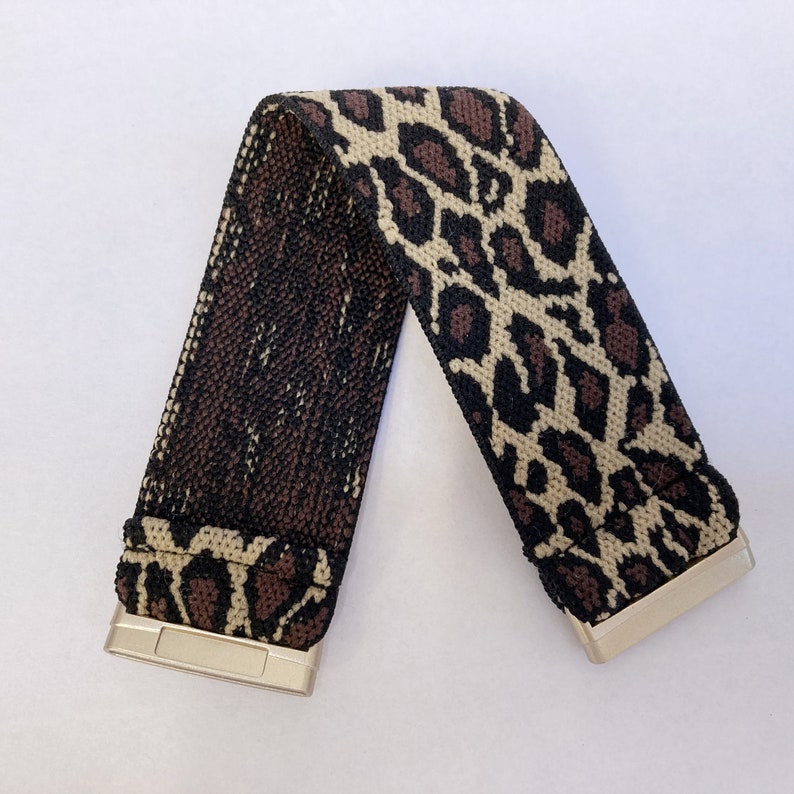 Puede incluir: Una diadema el&aacute;stica de estampado de leopardo marr&oacute;n y beige con una hebilla de metal dorado.