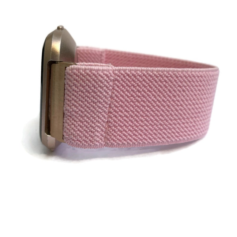 May include: A pink elastic watch strap with a gold metal watch face.