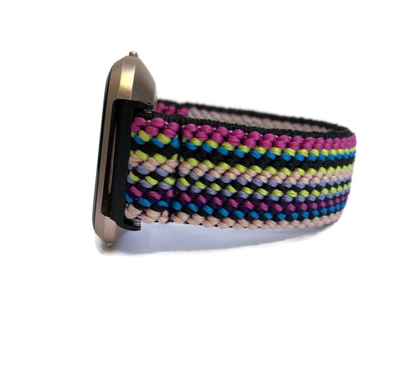 May include: A colourful woven watch band with pink, blue, green and black stripes. The band is attached to a rose gold smartwatch.