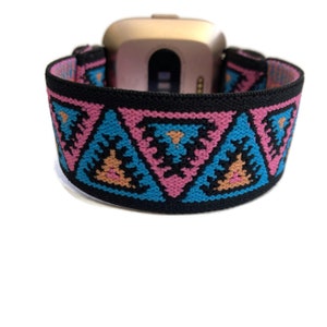 May include: A black elastic watch band with a geometric pattern of pink, blue, and orange triangles. The band is designed to fit a smartwatch.