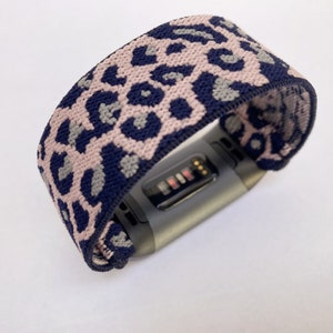 Op de afbeelding: Een zwarte fitness tracker met een roze en blauwe luipaardprint band.