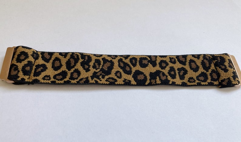 May include: A brown and black leopard print elastic belt with gold metal ends.