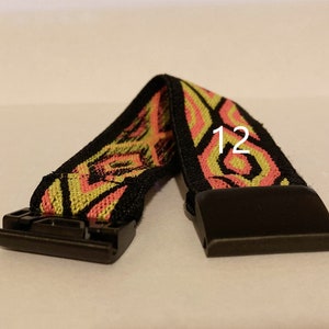 Op de afbeelding: Een zwart en geel gepatroneerd horlogebandje met een zwarte gesp. Het bandje heeft een roze en geel geometrisch ontwerp. Het getal "12" is op het bandje gedrukt.