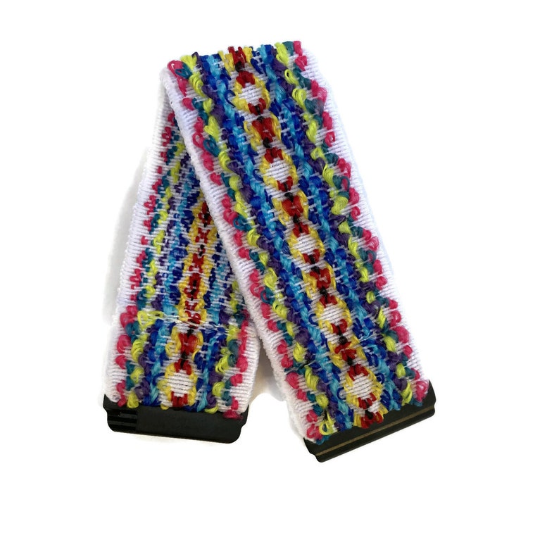May include: A white elastic band with a colourful woven pattern in shades of red, yellow, blue, green, and purple. The band has black plastic clasps on each end.
