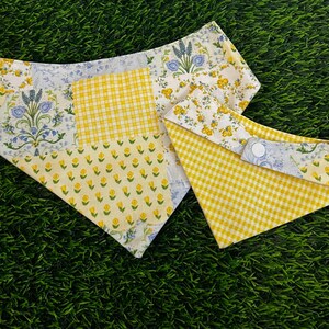 May include: Two triangular pet bandanas featuring a patchwork design of yellow gingham, small yellow floral patterns, and blue botanical prints on a white background. Each bandana includes a white plastic snap fastener for secure closure.