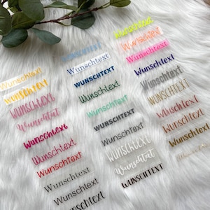 Könnte beinhalten: Eine Sammlung transparenter Aufkleber mit dem Wort "Wunschtext" in verschiedenen Farben, darunter Pink, Blau, Grün, Gelb und Weiß.