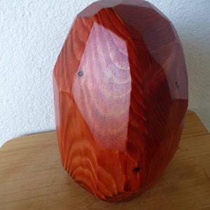 Könnte beinhalten: Eine große, rote Holzskulptur mit geometrischem, facettiertem Design. Die Skulptur ist aus Holz gefertigt und hat eine glatte, polierte Oberfläche.