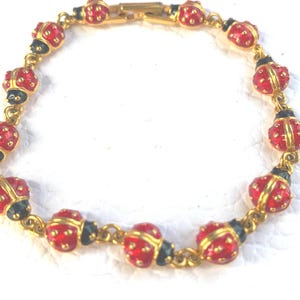 May include: Gold-coloured bracelet featuring red ladybug charms with black and gold accents. The ladybugs are detailed with small red dots. The bracelet is linked with gold-coloured chain links and has a clasp closure.