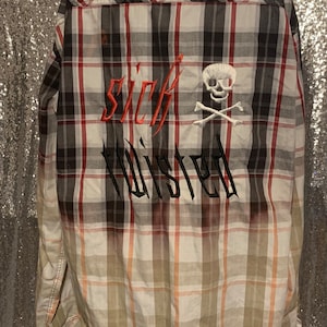 May include: A long-sleeved plaid shirt with a faded ombre effect. The shirt has a white skull and crossbones design with the words "sick twisted" embroidered on the back.