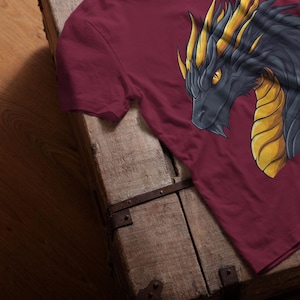 Peut inclure: Un t-shirt bordeaux avec un motif de tête de dragon noir et or. Le dragon a une expression féroce et des dents acérées.