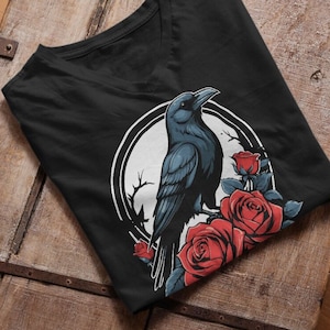 Può includere: Maglietta nera con una grafica di un corvo nero appollaiato su un ramo con rose rosse. Il corvo è circondato da un cerchio bianco con un ramo bianco dietro.