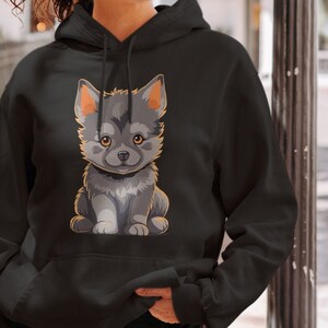 Könnte beinhalten: Ein schwarzer Hoodie mit einem Cartoon-Bild eines grau-weißen Welpen mit braunen Augen. Der Welpe sitzt auf seinen Hinterbeinen mit gekreuzten Pfoten.