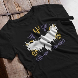 Op de afbeelding: Zwart T-shirt met een wit en geel grafisch ontwerp met abstracte vormen en symbolen. Het ontwerp heeft een distressed, verfspatter effect. Het shirt is gemaakt van een zacht materiaal en is geschikt voor casual wear.