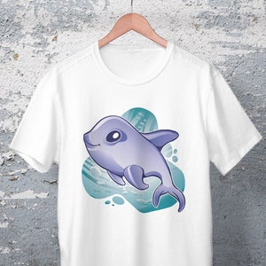 Op de afbeelding: Wit T-shirt met een cartoonillustratie van een paarse dolfijn die in blauw water zwemt.