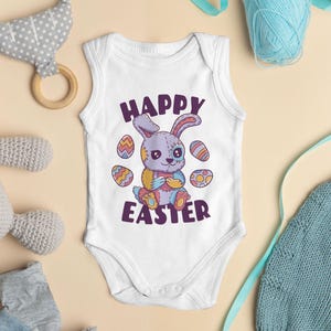 Könnte beinhalten: Weißer Baby-Strampler mit einem lila Hasen, der ein buntes Osterei hält. Der Strampler hat den Text "Happy Easter" aufgedruckt.