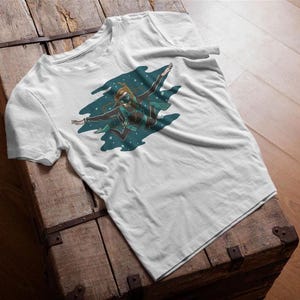 Op de afbeelding: Wit t-shirt met een afbeelding van een persoon in een duikpak, met uitgestrekte armen, tegen een blauwgroene achtergrond. Het ontwerp is gecentreerd. Het shirt wordt gepresenteerd op een houten kist.
